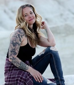 Colorado Springs Massage Therapist by popular Colorado Springs Massage Therapist, Camino Massage: image of a woman with a arm sleeve tattoo and wearing a black tank top, paid button up shirt, and jeans.