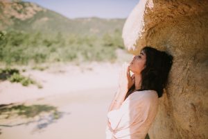 Massage Therapist by popular Colorado Springs Massage Therapist, Camino Massage: image of a woman leaning against a rock formation and wearing a cream wrap top and olive leggings. 